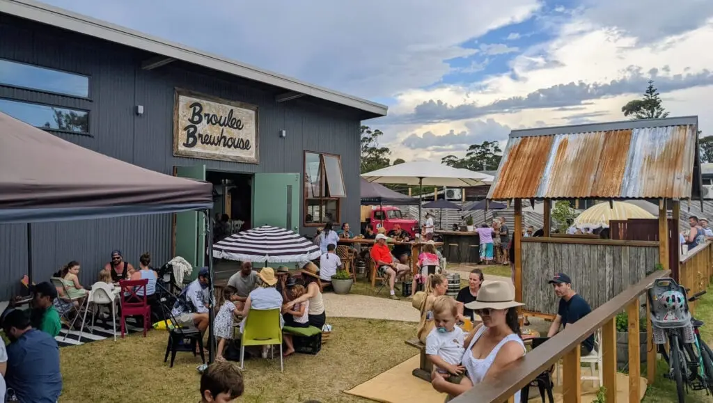 Visitors relax in the outdoor beer garden at Broulee Brewhouse, with families and groups gathered around picnic tables on a sunny afternoon. The venue is a popular stop for craft beer South Coast travellers looking to enjoy locally brewed beers in a relaxed coastal setting.