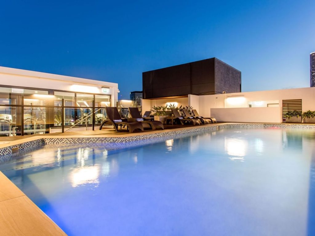 Rooftop pool at Hotel Grand Chancellor Brisbane surrounded by lounge chairs and softly lit terraces at dusk. The spacious outdoor swimming pool offers a relaxing retreat above central Brisbane.