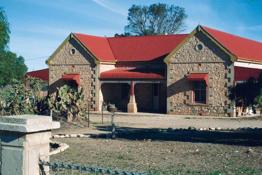 Historic stone building at Balladonia Station with a bright red corrugated roof and cactus plants outside. The station is a rustic stop on a road trip from Brisbane to Perth across Australia.