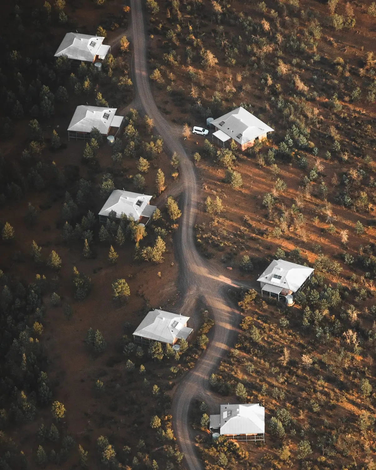 Aerial view of luxury eco villas spaced among native bushland at Rawnsley Park Station with a winding gravel road between them. A secluded accommodation option for a Flinders Ranges camping trip.