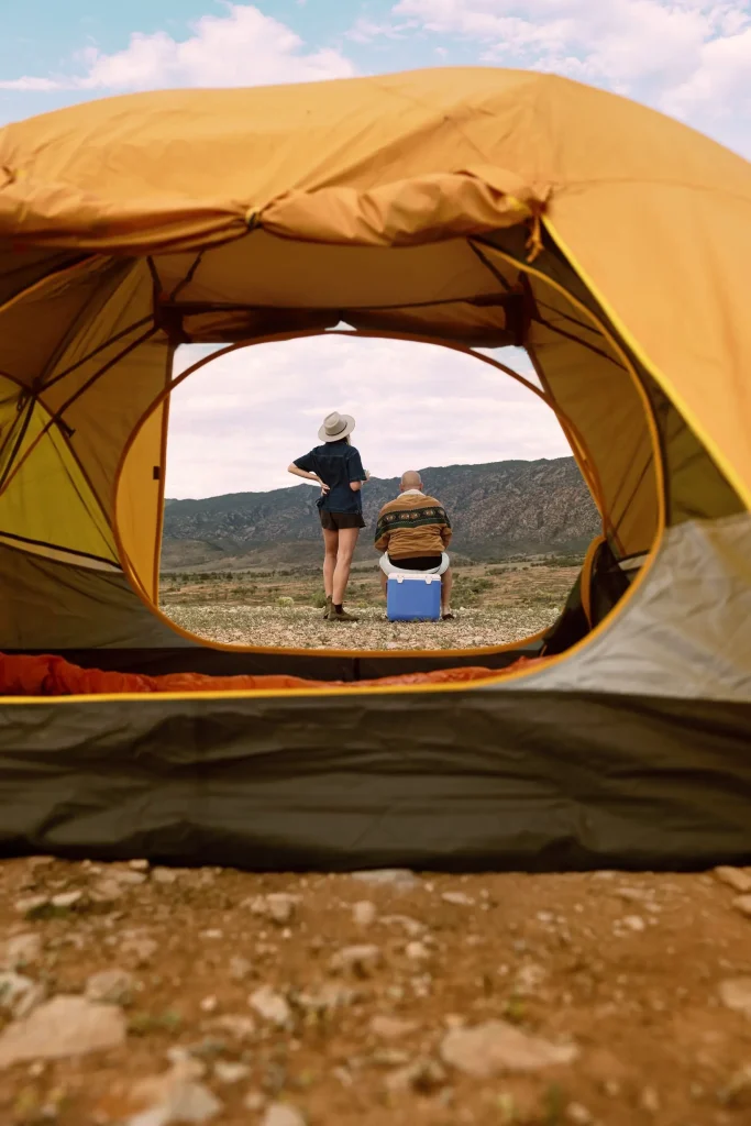 View through an open tent toward two campers looking across the rugged mountains at Mount Little Station. A peaceful Flinders Ranges camping spot surrounded by outback scenery.