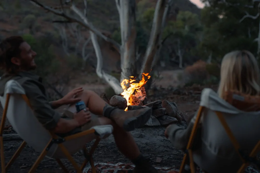 Two campers relax in chairs beside a glowing campfire among the gum trees at Parachilna Gorge. A cozy evening at one of the scenic camping spots in the Flinders Ranges.