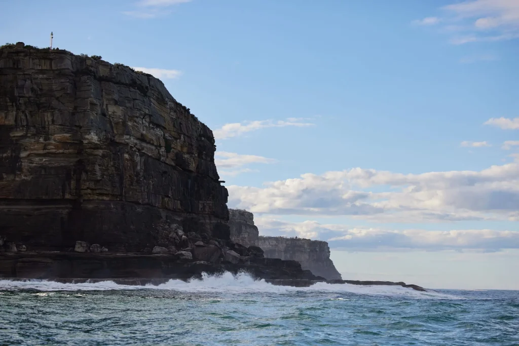 Waves crash against the towering sandstone cliffs at The Gap on Sydney coastline. The dramatic headland overlooks waters where you can see migrating whales.