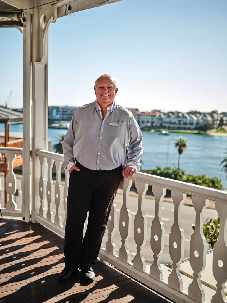 A smiling staff member on the white timber balcony of Tradewinds Hotel overlooking the Swan River in East Fremantle, one of the best hotels near Perth with a pool
